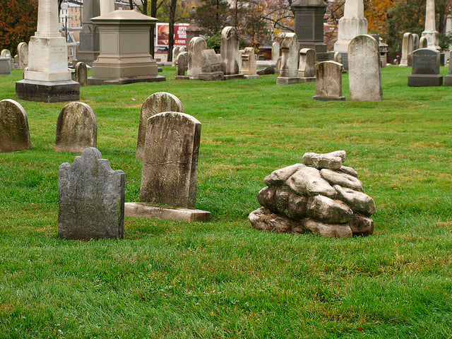 Old headstones in a cemetery with green grass and a small pile of rocks.